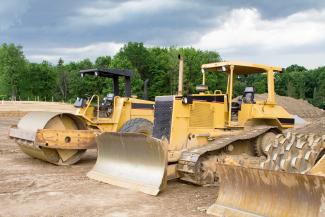 Earth moving equipment sitting in cleared area with stakes and trees in background